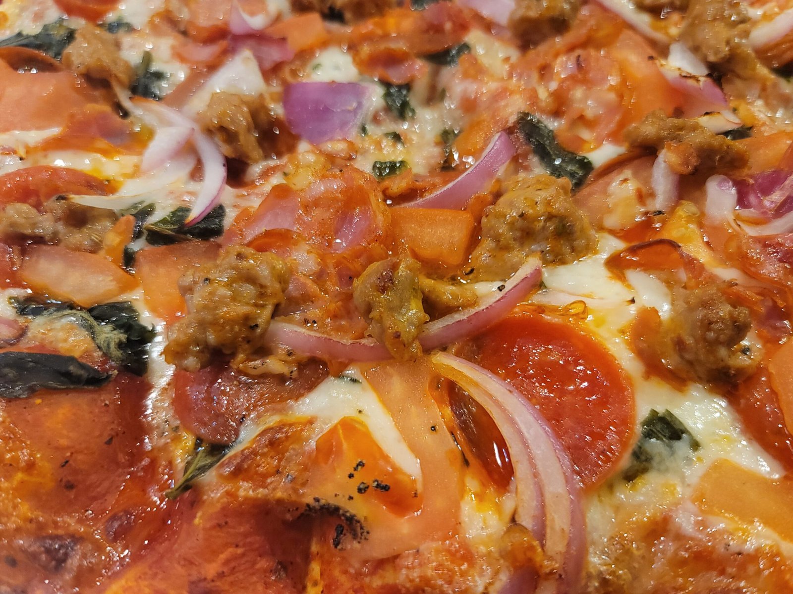 Close-up of a Firehouse pizza loaded with pepperoni, sausage, onions, and vegetables